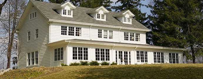 The back of a large white manor with many windows surrounded by trees.